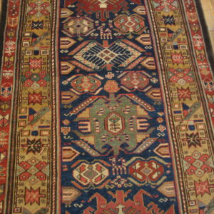 Traditional runner rug with complex geometric motifs in navy blue, rust, green, and tan on wood planks.