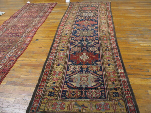Two runner rugs, one navy and red geometric, the other red-toned, lie on a light wood floor.