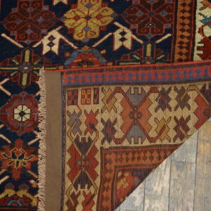 A deep blue and red geometric rug with fringes is folded back on distressed gray wood flooring.
