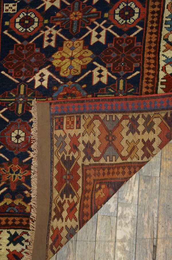 A deep blue and red geometric rug with fringes is folded back on distressed gray wood flooring.