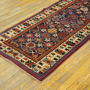 Low-pile navy runner with complex red and ivory geometric designs lies on rustic hardwood flooring.