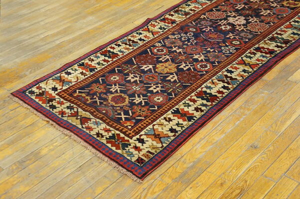 Low-pile navy runner with complex red and ivory geometric designs lies on rustic hardwood flooring.