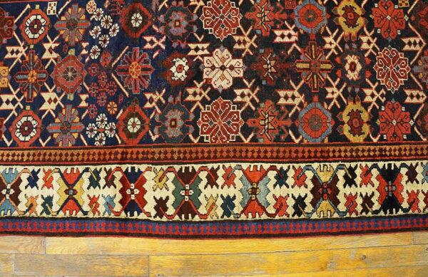 A traditional rug with complex navy, red, and cream geometric patterns rests on yellow wood flooring.