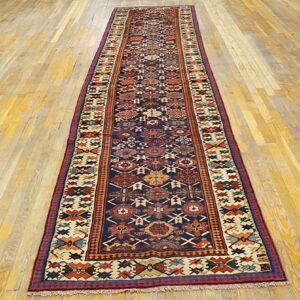 Long runner rug featuring a detailed geometric pattern on a navy blue field over light wood planks.