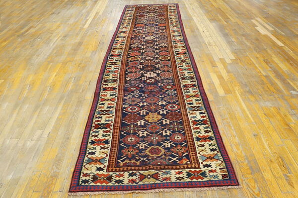 Long runner rug featuring a detailed geometric pattern on a navy blue field over light wood planks.