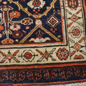 Detailed navy rug corner with cream, rust, and brown geometric patterns on light plank wood flooring.