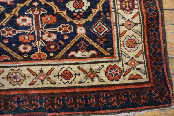 Detailed navy rug corner with cream, rust, and brown geometric patterns on light plank wood flooring.