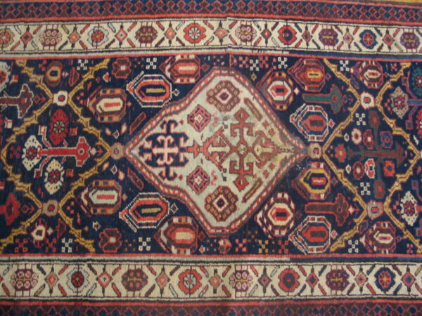 Navy blue rug with a central cream diamond medallion and geometric red and gold tribal patterns.