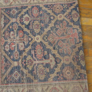 Low-pile geometric rug in navy, tan, and red covers a distressed golden hardwood floor.