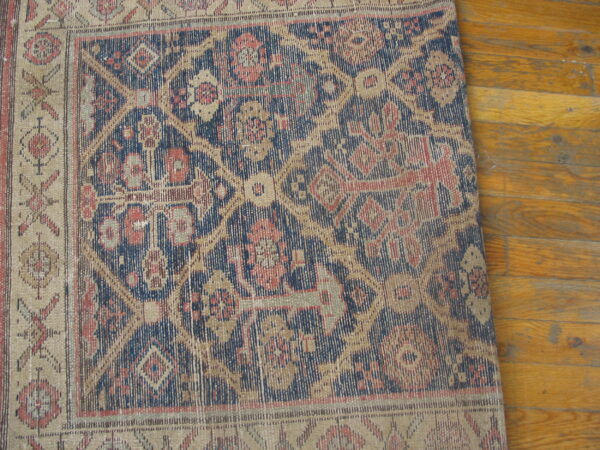 Low-pile geometric rug in navy, tan, and red covers a distressed golden hardwood floor.