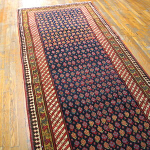 Navy runner rug with red and gold geometric motifs and layered borders rests on light hardwood floors.