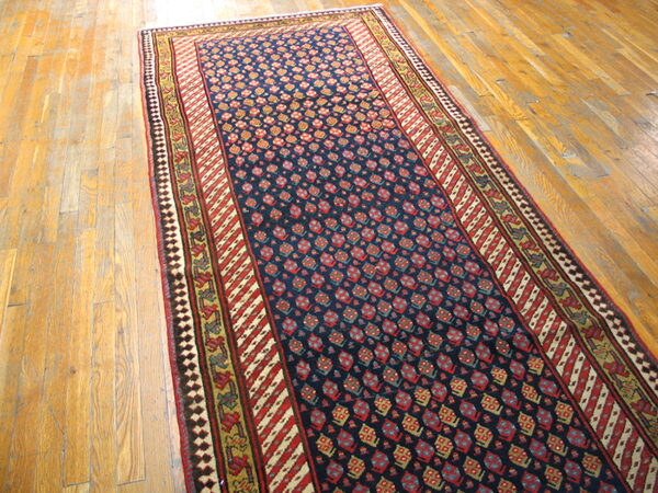 Navy runner rug with red and gold geometric motifs and layered borders rests on light hardwood floors.