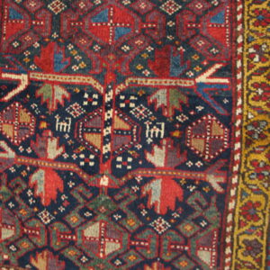 Close-up of a tribal rug with navy, red, and green geometric motifs and a dense yellow border.
