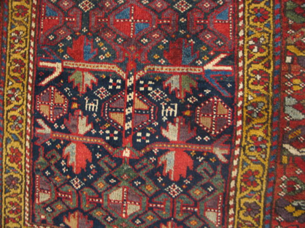 Close-up of a tribal rug with navy, red, and green geometric motifs and a dense yellow border.