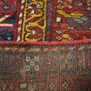 Close detail of a patterned rug edge showing the colorful pile and the tight geometric weave of the backing.