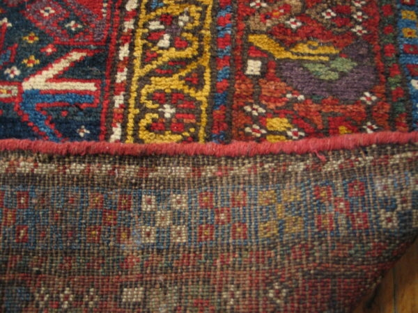 Close detail of a patterned rug edge showing the colorful pile and the tight geometric weave of the backing.
