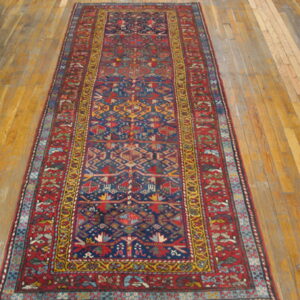 Runner rug with a navy blue field, red borders, and geometric designs rests on wide hardwood planks.