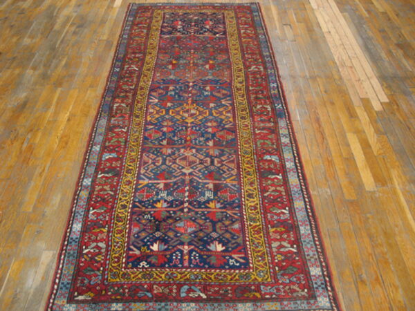Runner rug with a navy blue field, red borders, and geometric designs rests on wide hardwood planks.