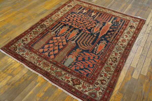 Geometric rug featuring navy and salmon red motifs, bordered in beige and red, resting on light wood floors.