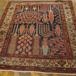 Low-pile rug with a blue field, red tree pattern, and intricate tan borders on hardwood floors.
