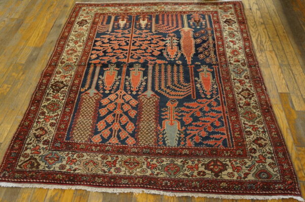 Low-pile rug with a blue field, red tree pattern, and intricate tan borders on hardwood floors.