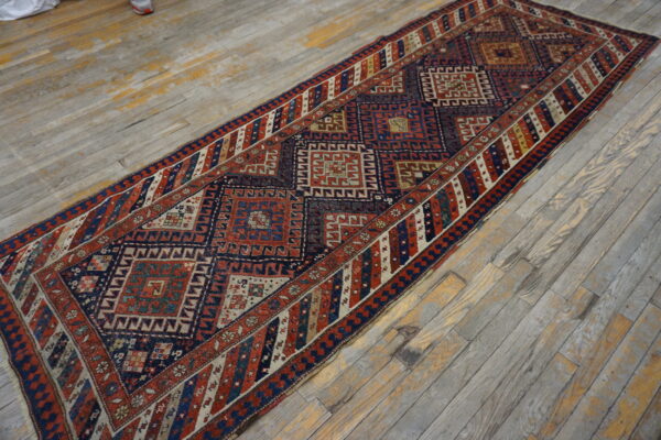 Tribal runner rug in rust and navy with geometric diamonds on distressed gray wood planks.