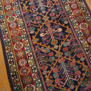 Geometric runner rug with a dark blue central field and multi-colored patterned borders on light wood flooring.