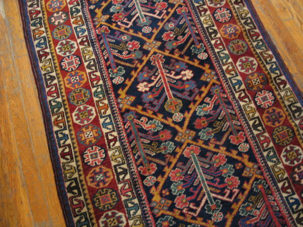 Geometric runner rug with a dark blue central field and multi-colored patterned borders on light wood flooring.