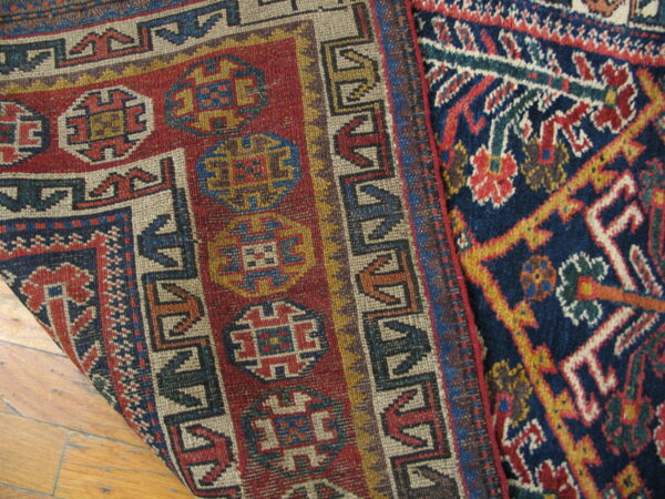 Two low-pile rugs with bold geometric patterns in red, navy, and tan rest on a wood floor.