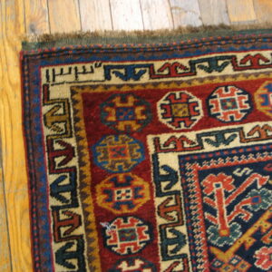 Geometric patterned rug corner in red, navy, and cream, showing short pile on plank hardwood.