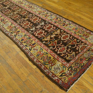 Geometric runner rug in dark brown, red, and gold, centered on shiny wood plank flooring.