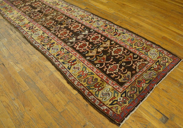 Geometric runner rug in dark brown, red, and gold, centered on shiny wood plank flooring.