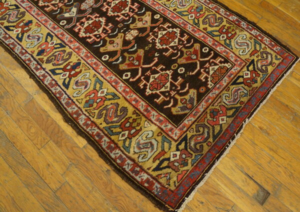 Geometric rug featuring a dark central field and a wide mustard yellow border sits on wooden floorboards.