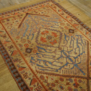 Geometric tan rug with stylized blue and rust patterns lies on a muted tan surface and distressed wood floor.