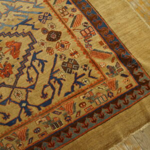 A tan rug with blue and terracotta geometric patterns lies on distressed light brown wood flooring.