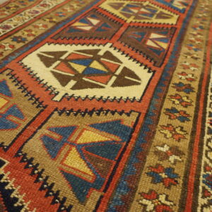 Low-pile tribal rug featuring alternating geometric and floral motifs in earthy red, blue, and tan colors.