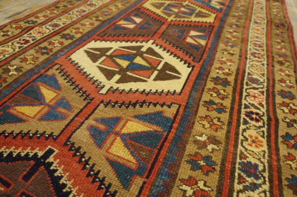 Low-pile tribal rug featuring alternating geometric and floral motifs in earthy red, blue, and tan colors.