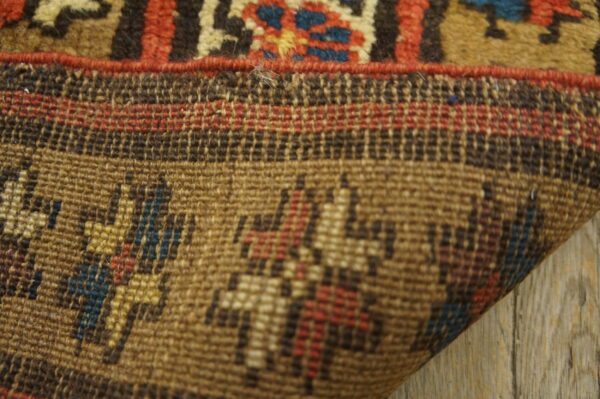 Knotted rug edge showing low pile brown, red, and blue pattern next to the flat woven foundation.