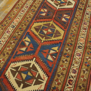 Geometric runner rug in red, blue, and gold on distressed light wooden floorboards.