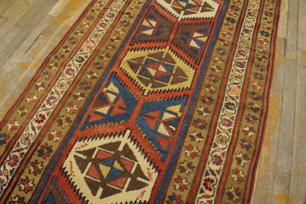 Geometric runner rug in red, blue, and gold on distressed light wooden floorboards.