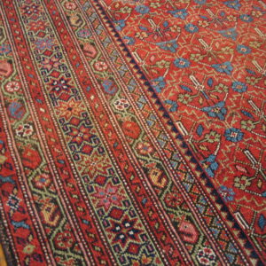 Low-pile red rug featuring multi-striped borders and a densely patterned field on hardwood floors.