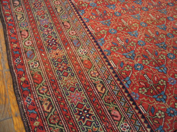 Low-pile red rug featuring multi-striped borders and a densely patterned field on hardwood floors.