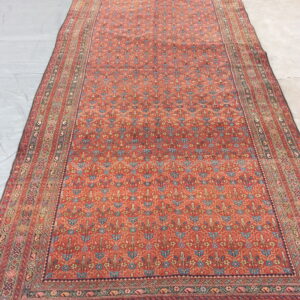 Long red and blue low-pile area rug with complex tribal repeating patterns displayed on a concrete floor.