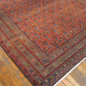 Traditional low-pile rug with a dense red field and multi-colored border on wide wood planks.