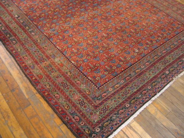 Traditional low-pile rug with a dense red field and multi-colored border on wide wood planks.
