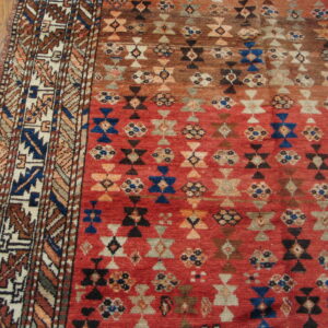 Red and brown geometric rug with blue accents and an elaborate border on hardwood planks.