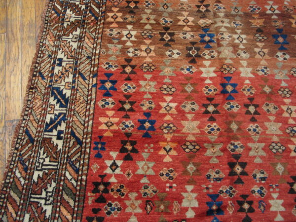 Red and brown geometric rug with blue accents and an elaborate border on hardwood planks.