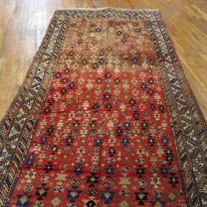 Red runner rug featuring detailed navy and cream geometric patterns laid on a glossy wood floor.