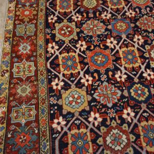 Navy and rust geometric rug with detailed medallions rests on distressed wooden floorboards.