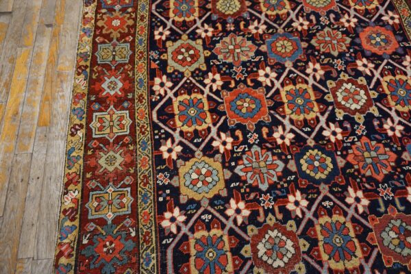 Navy and rust geometric rug with detailed medallions rests on distressed wooden floorboards.